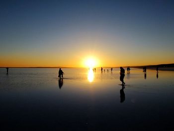 Silhouette people on beach against sky during sunset