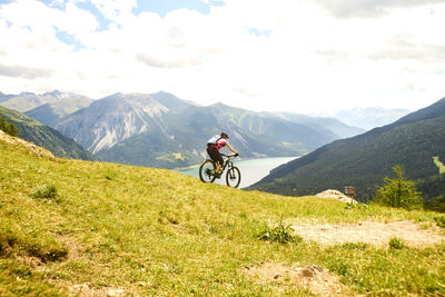 Woman riding bicycle on mountain against sky