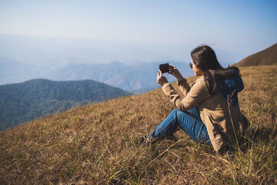 Asian woman traveler is sitting and take pictures of the mountains with a mobile phone