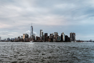 Sea by modern buildings in city against sky