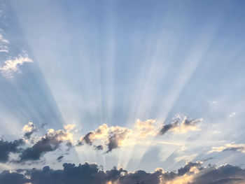 Low angle view of sunlight streaming through clouds