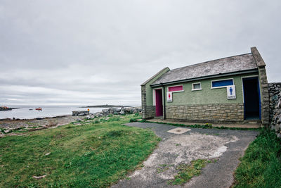 Built structure on grass by sea against sky