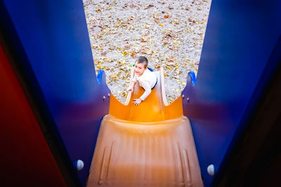 High angle portrait of boy sitting on slide in playground