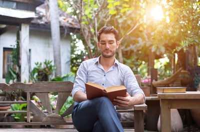 Young man sitting on seat against trees