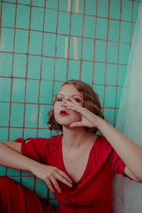 Close-up of young woman in red dress gesturing against wall