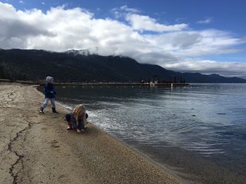 Children playing by lake tahoe against cloudy sky