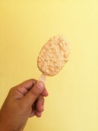 Hand holding ice cream cone against yellow background