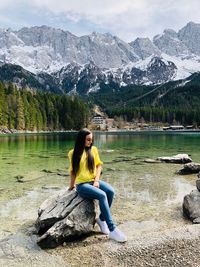 Woman sitting on rock by lake against mountains