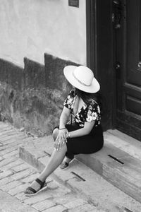 Full length of woman wearing hat while sitting against building