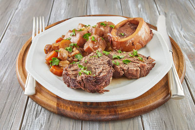 Ossobuco with vegetables on plate with knife and fork on wooden background