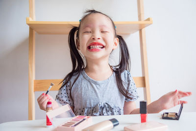 Smiling girl wearing lipstick while sitting at table in home