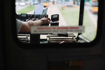 Cropped hand of driver driving bus seen through window