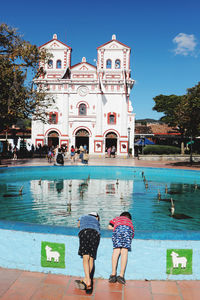 Rear view of people on swimming pool against blue sky