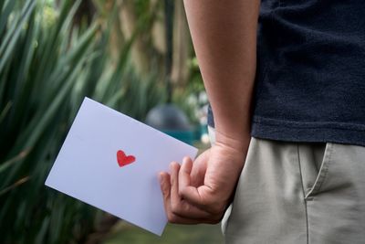 Midsection of man holding paper with red heart shape