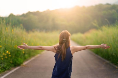 Rear view of woman with arms raised standing on road