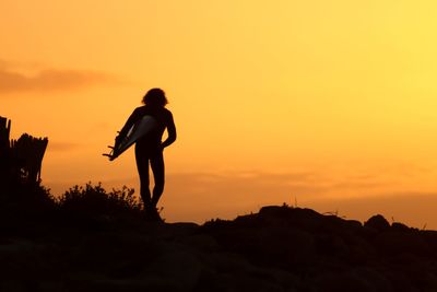 Silhouette man standing on rock against orange sky