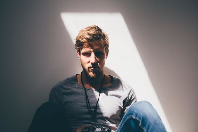 Sunlight falling on young man sitting by white wall