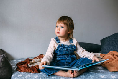 Full length of girl holding book while sitting on bed