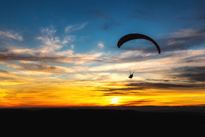 Silhouette person paragliding against sky during sunset