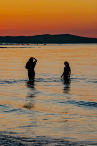 Silhouette people in sea against sky during sunset