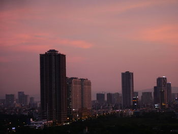 Illuminated buildings in city against sky during sunset