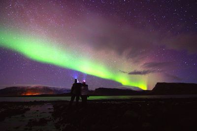 Rear view of couple against aurora in sky at night