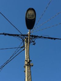 Low angle view of electricity cables on street light against clear blue sky