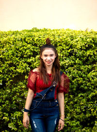 Portrait of a smiling young woman standing against plants