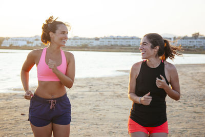 Smiling female friends talking while jogging at beach
