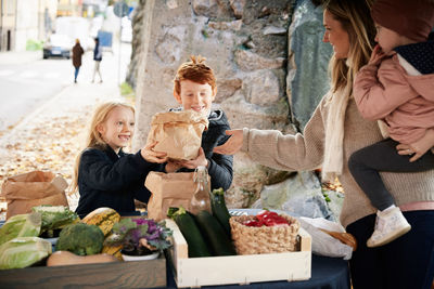 Smiling male and female sibling buying vegetables from female market vendor