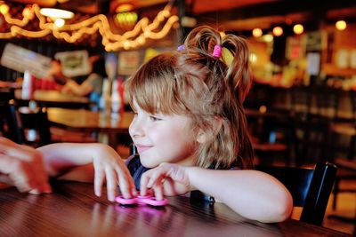 Close-up of smiling girl holding fidget spinner at table in restaurant