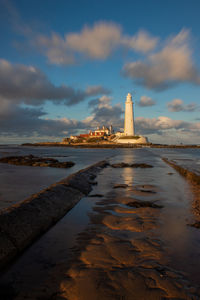 Lighthouse on beach by sea against sky during sunset