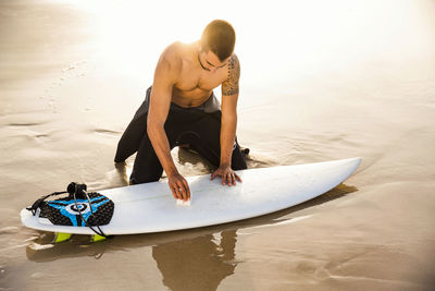 Man applying wax on surfboard at beach