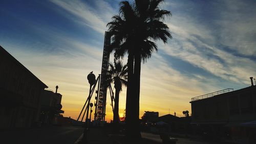 Low angle view of silhouette palm trees and buildings against sky during sunset