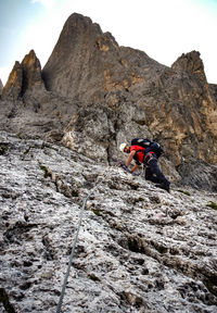 Low angle view of man climbing on mountain against sky