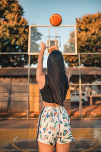 Woman in black top and floral shorts playing basketball.
