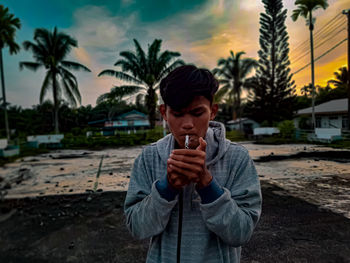 Portrait of young man standing against palm trees