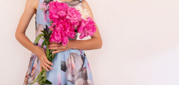 Midsection of woman holding pink flower against white background
