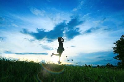 Low angle view of woman jumping on grassy field during sunset