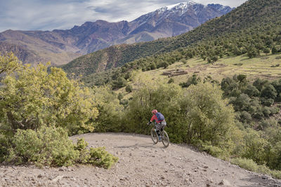 Rear view of man riding bicycle on road against mountains and sky