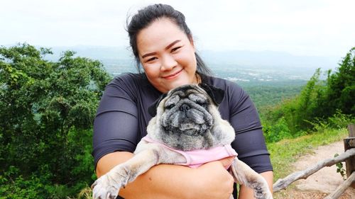 Portrait of woman holding dog while standing against landscape