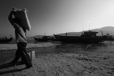 Man carrying bag of ice to fishing boat moored on beach