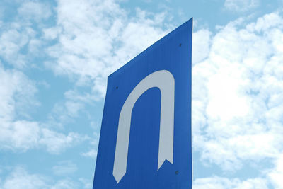 Low angle view of u-turn road sign against cloudy sky