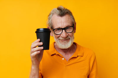 Young woman drinking water against yellow background