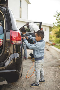 Full length of boy charging electric car while standing on driveway