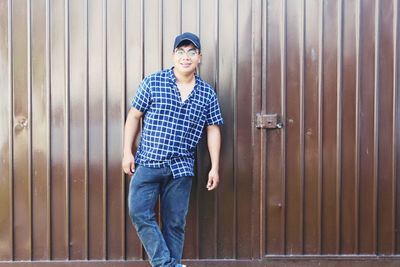 Portrait of young man standing against brown corrugated iron