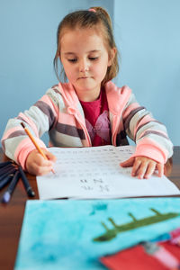 Cute girl writing in book on table at home