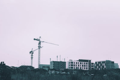 Low angle view of crane by building against clear sky