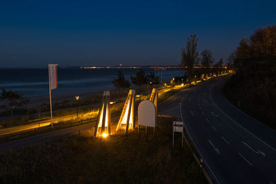 Illuminated road by bridge against sky at night