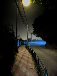 Empty road by trees against sky at night